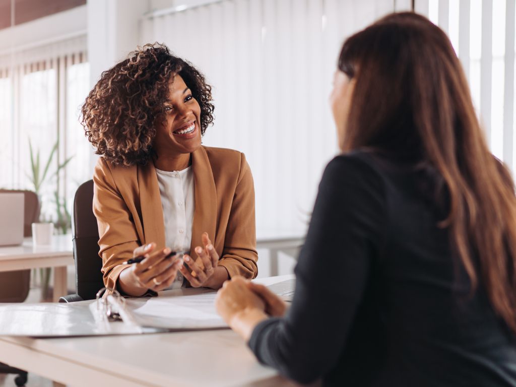 Succession Planning Isn’t Just For Big Companies- Here’s Why Your Small Business Needs One 6 Two women engaged in conversation at a desk in a modern office setting.
