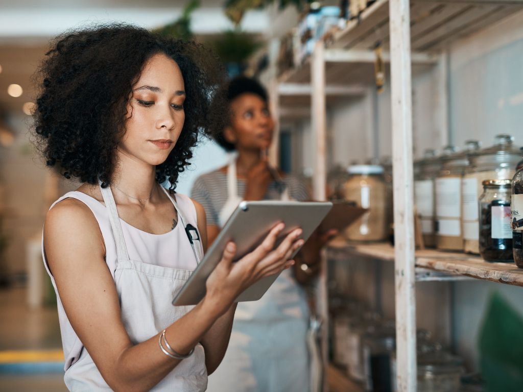 Succession Planning Isn’t Just For Big Companies- Here’s Why Your Small Business Needs One 2 A woman with curly hair holds a tablet while standing near shelves filled with jars of various ingredients in a well-lit store.